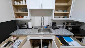 A kitchen with a granite countertop, stainless steel sink, and white cabinets.