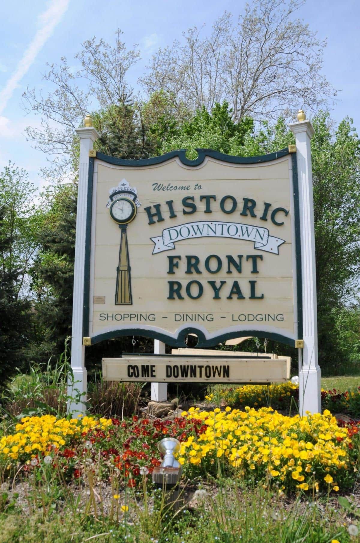 A historic downtown front royal sign with a clock, surrounded by colorful flowers.
