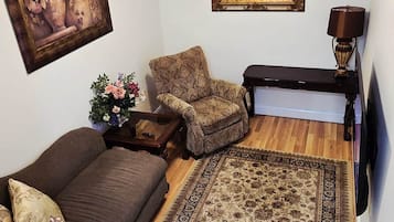 A living room with a brown sofa, a patterned armchair, a wooden coffee table, a large rug, a ceiling fan, a framed picture, and a lamp.