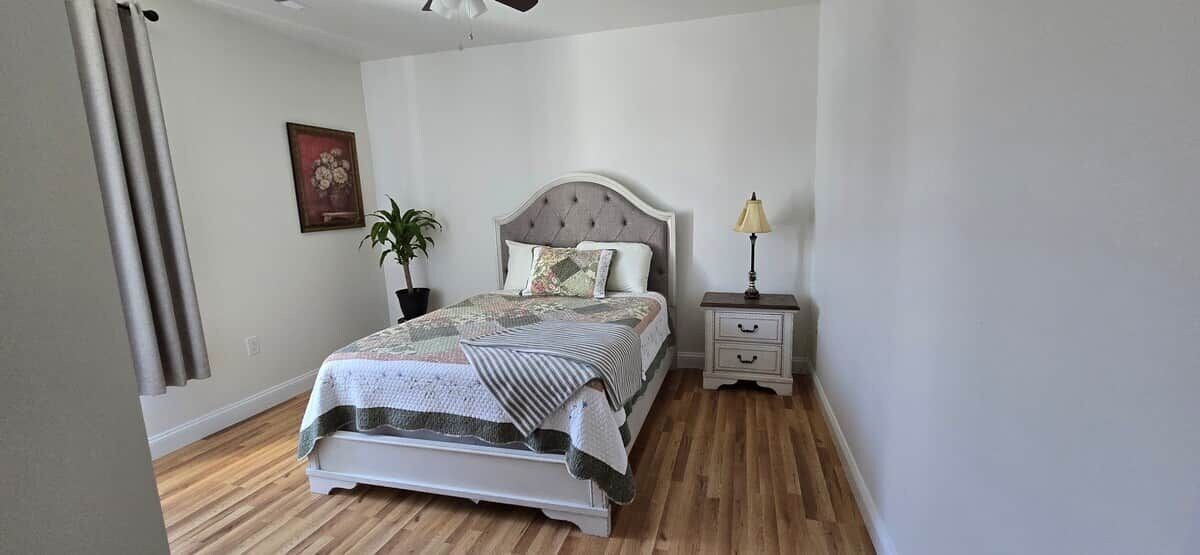 A bedroom with a bed, bedside table, lamp, and a potted plant.