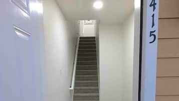 Un pasillo que conduce a una escalera, con piso alfombrado y una puerta a la izquierda.