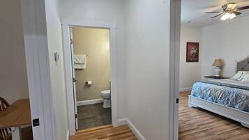 A bedroom with a bed, a nightstand, a ceiling fan, and a bathroom visible through an open door.