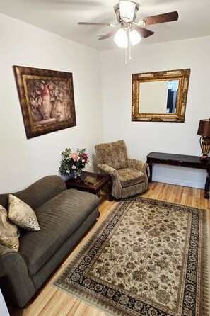 Un salon comprenant un canapé, un fauteuil, une table basse, un tapis, un ventilateur de plafond et un miroir.