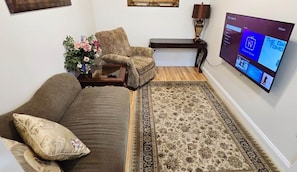 Un salon comprenant un canapé, un fauteuil, une table basse et un téléviseur à écran plat fixé au mur.