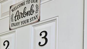 Eine weiße Tür mit einem Schild, auf dem 'Welcome to our Airbnb Enjoy your stay' steht, und den Zahlen '2' und '3' als Zimmernummern.