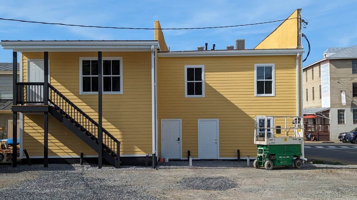 Un edificio amarillo con una escalera, una puerta y un vehículo pequeño verde.