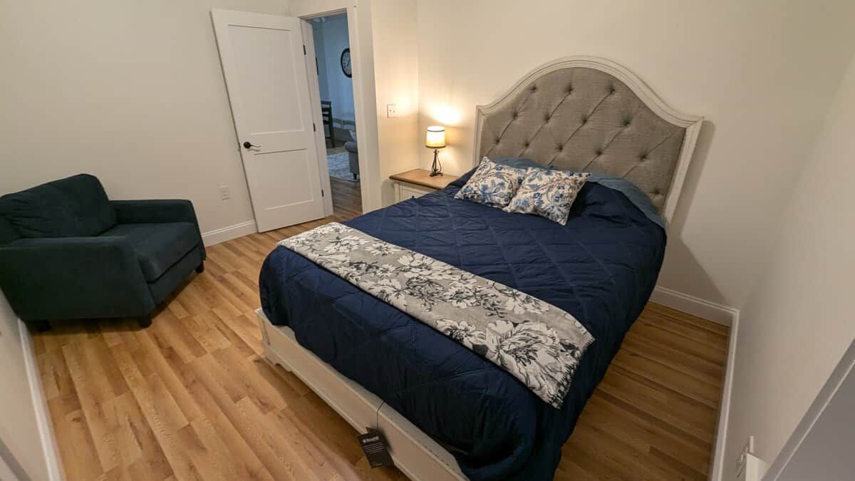 Een slaapkamer met een bed, een nachtkastje, een lamp en een groene stoel.