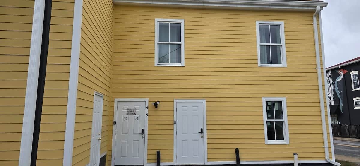 A two-story yellow building with white trim, two doors, and two windows.