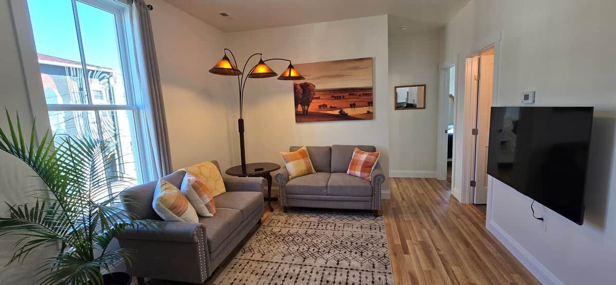 Una sala de estar con sofá, sillón, lámpara de pie y televisor de pantalla plana.