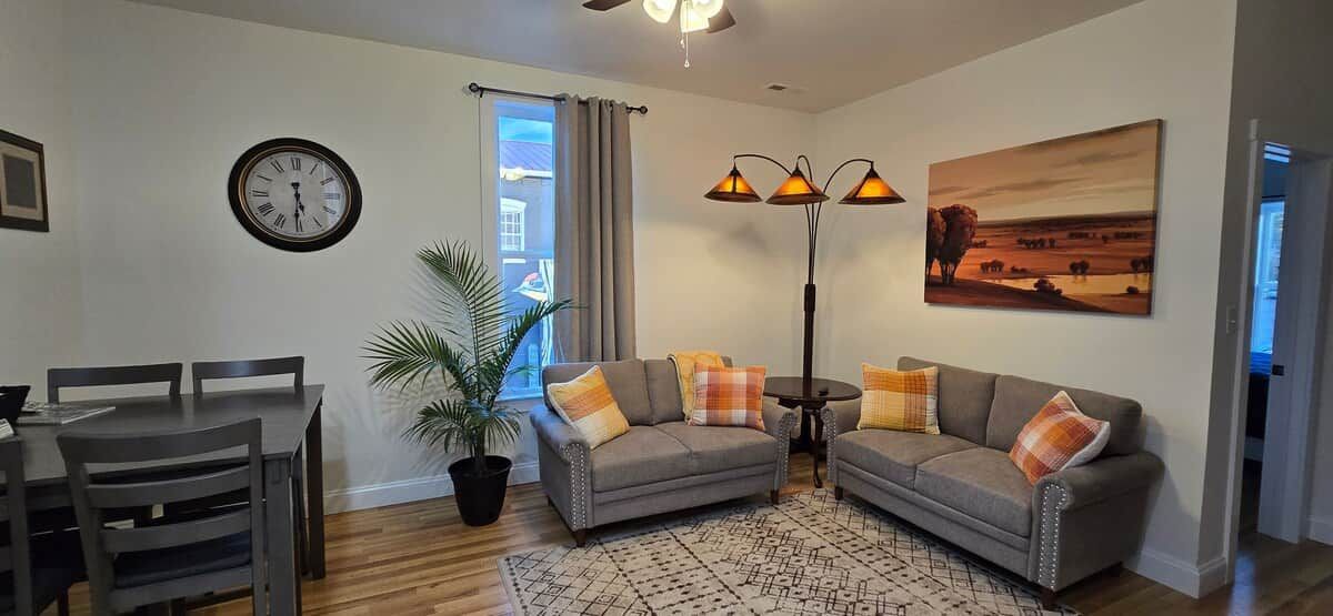 A living room with a dining table, two sofas, a floor lamp, a clock, and a window with curtains.