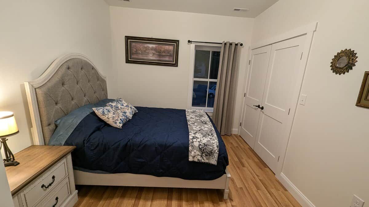 Un dormitorio con cama, mesita de noche, ventana con cortinas y puerta.