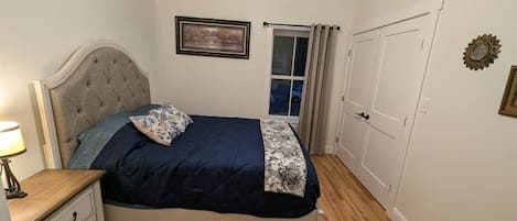 Un dormitorio con cama, mesita de noche, ventana con cortinas y puerta.
