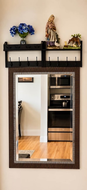 A kitchen with a built-in oven and a microwave, a decorative shelf with a figurine and flowers, and a mirror with a wooden frame.