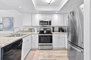 A modern kitchen with white cabinetry, stainless steel appliances, and a granite countertop. - The Beach Club Retreat (St. Augustine)