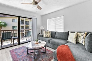 A modern living room with a grey sofa, a round coffee table, and a balcony with a view of a building. - The Beach Club Retreat (St. Augustine)
