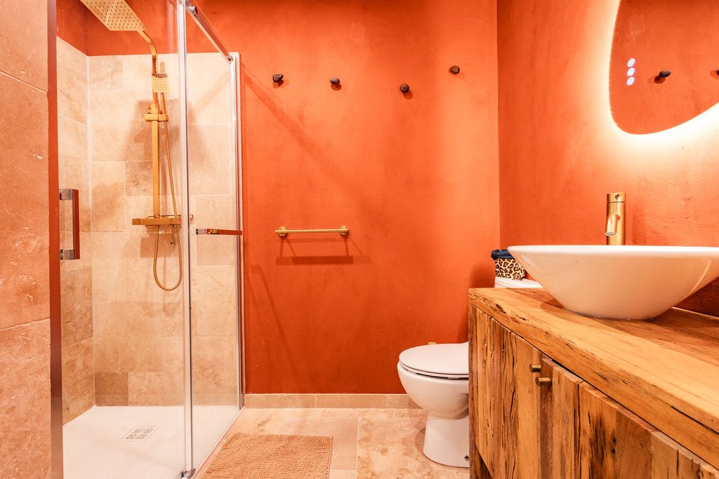 Une salle de bain avec une douche à parois de verre, des toilettes blanches et un meuble-lavabo en bois doté d’un grand lavabo blanc.