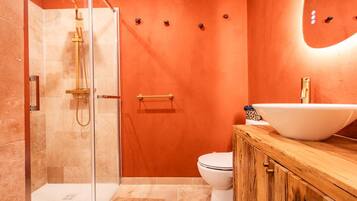 Une salle de bain avec une douche à parois de verre, des toilettes blanches et un meuble-lavabo en bois doté d’un grand lavabo blanc.