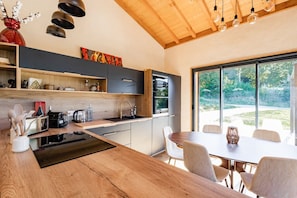 A modern kitchen with a wooden island, built-in appliances, and a dining area with a large window offering a view of the outdoors.