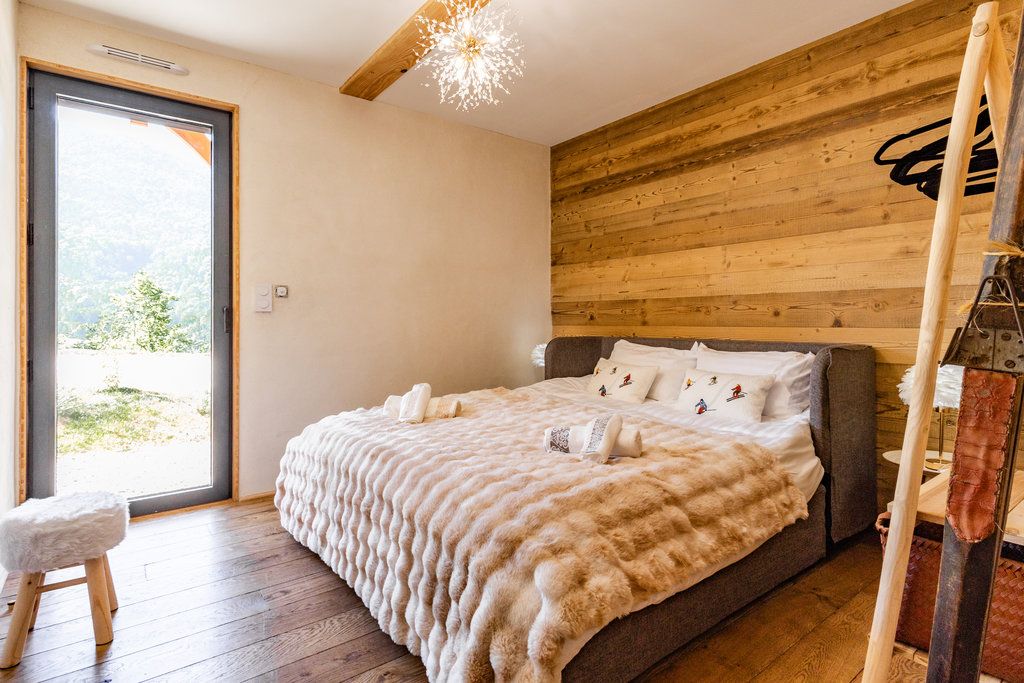 A bedroom with a large bed, wooden walls, a ceiling fan, and a view through a glass door.