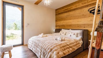 A bedroom with a large bed, wooden walls, a ceiling fan, and a view through a glass door.