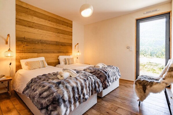 A bedroom with two beds, wooden paneling on the wall, and a view through a glass door.