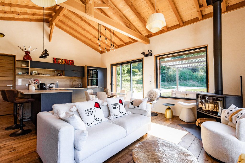 A modern living room with a sofa, a coffee table, and a fireplace. There is a kitchen area with a bar and a dining table.