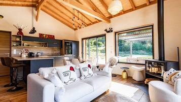 A modern living room with a sofa, a coffee table, and a fireplace. There is a kitchen area with a bar and a dining table.