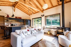 Una sala de estar moderna con sofá, mesa de centro y chimenea. Se observa una zona de cocina con barra y mesa de comedor.