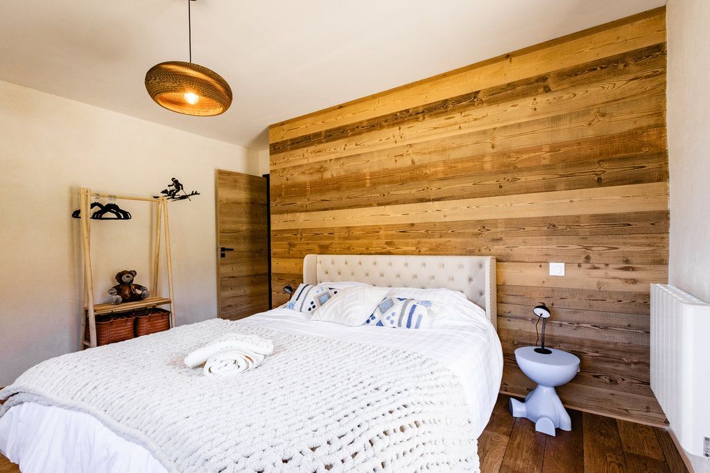 Une chambre à coucher avec une tête de lit en bois, un couvre-lit blanc, une table de chevet avec une lampe et un luminaire suspendu.