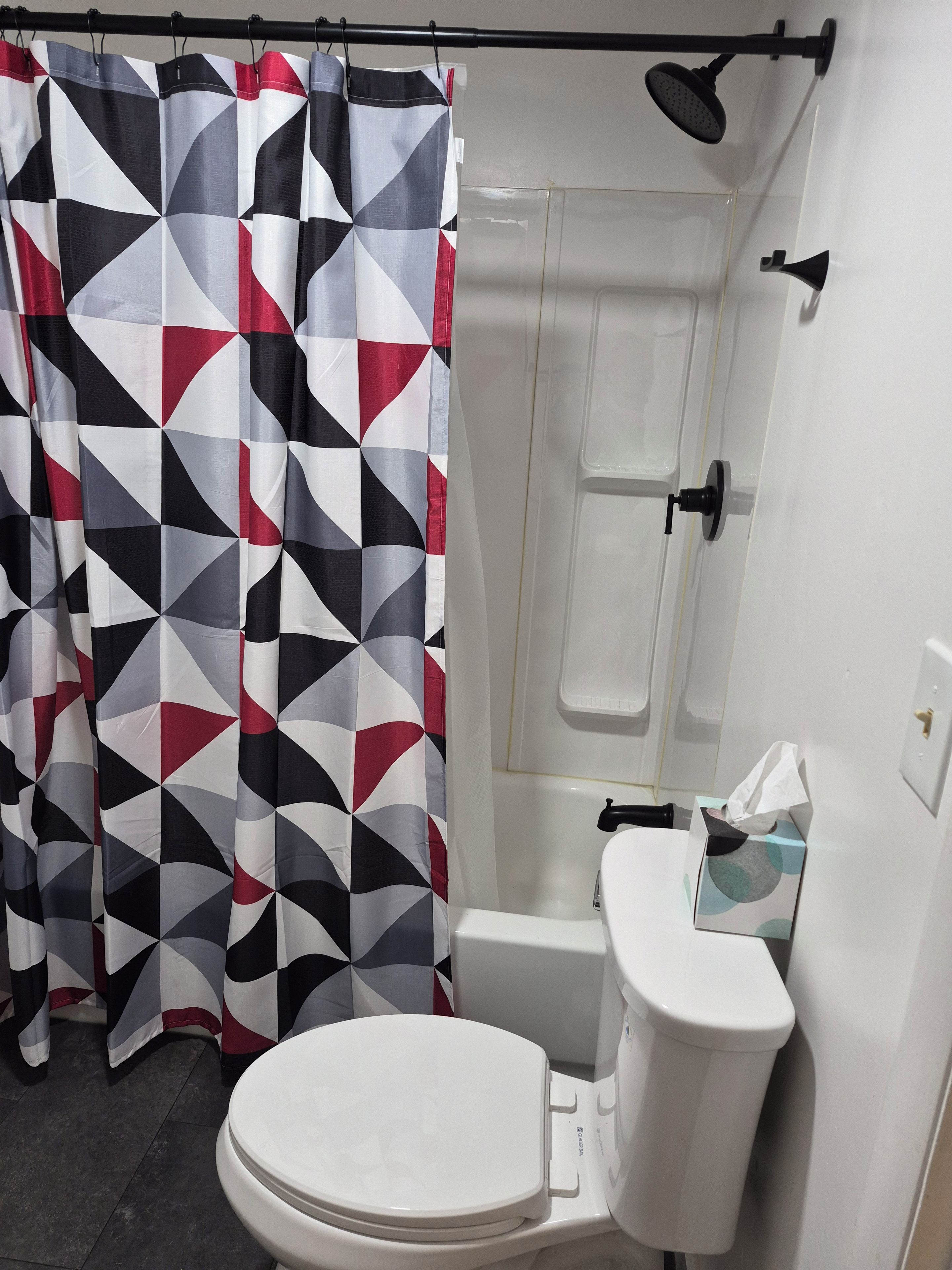 A bathroom with a geometric patterned shower curtain, a white toilet, and a shower enclosure.