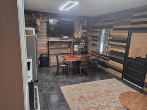 A compact kitchen with a dining area, a flat-screen TV, and a rustic wooden wall.