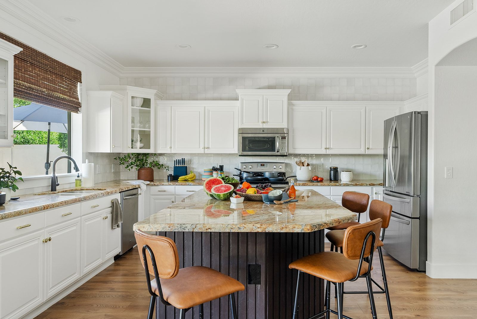 A modern kitchen with white cabinetry, a granite island, and stainless steel appliances.