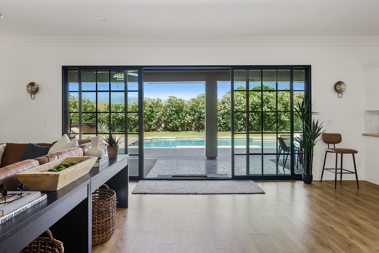 A modern living room with a large sliding glass door leading to a pool area, a wooden floor, and a seating area with a sofa and a coffee table.