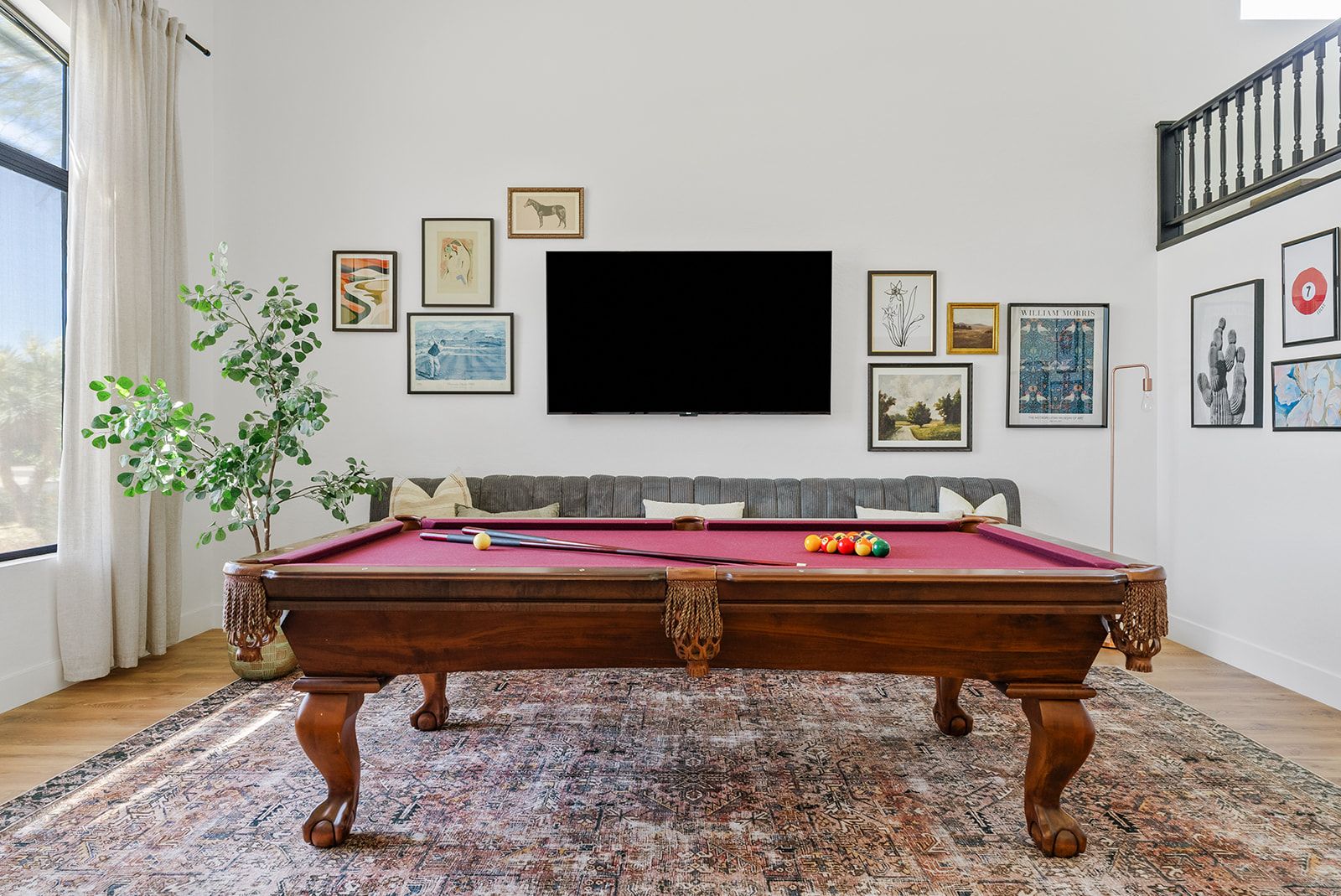 Een pooltafel in een kamer met een groot raam, een bank en diverse kunstwerken in lijsten aan de muren.