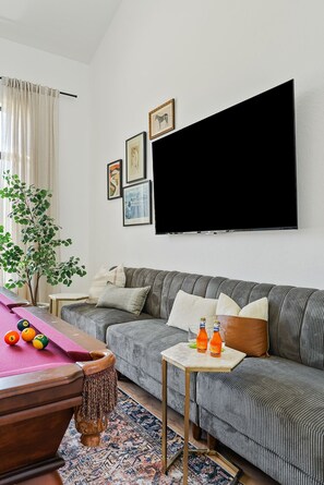 Ein Wohnzimmer mit einer Couch, einem Billardtisch, einem Flachbildfernseher und einem kleinen Tisch mit Flaschen.