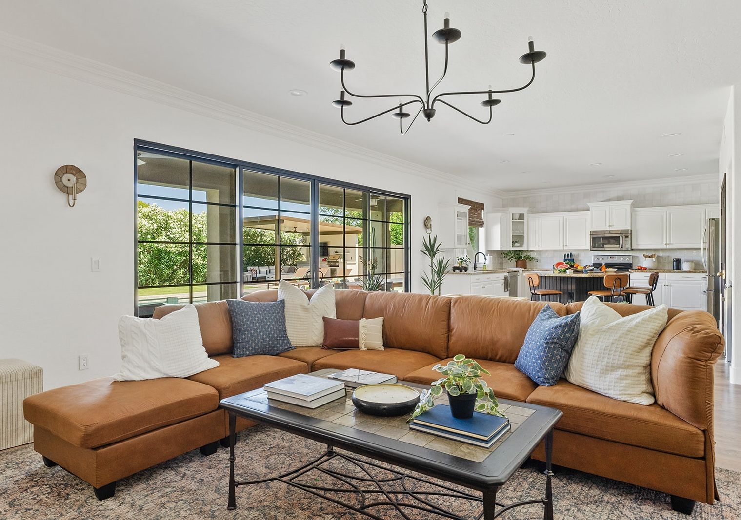 A modern living room with a sectional sofa, a coffee table, and a view of the kitchen and outdoor area.