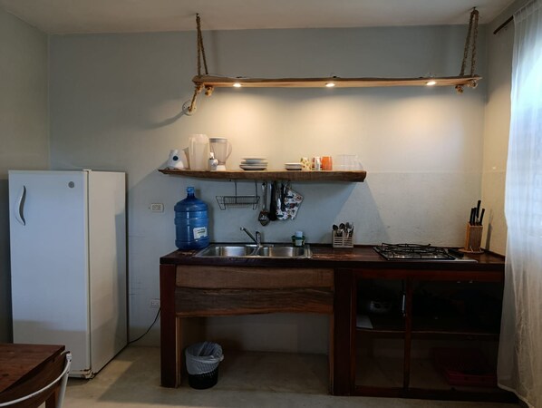A compact kitchen with a refrigerator, sink, and wooden countertop.