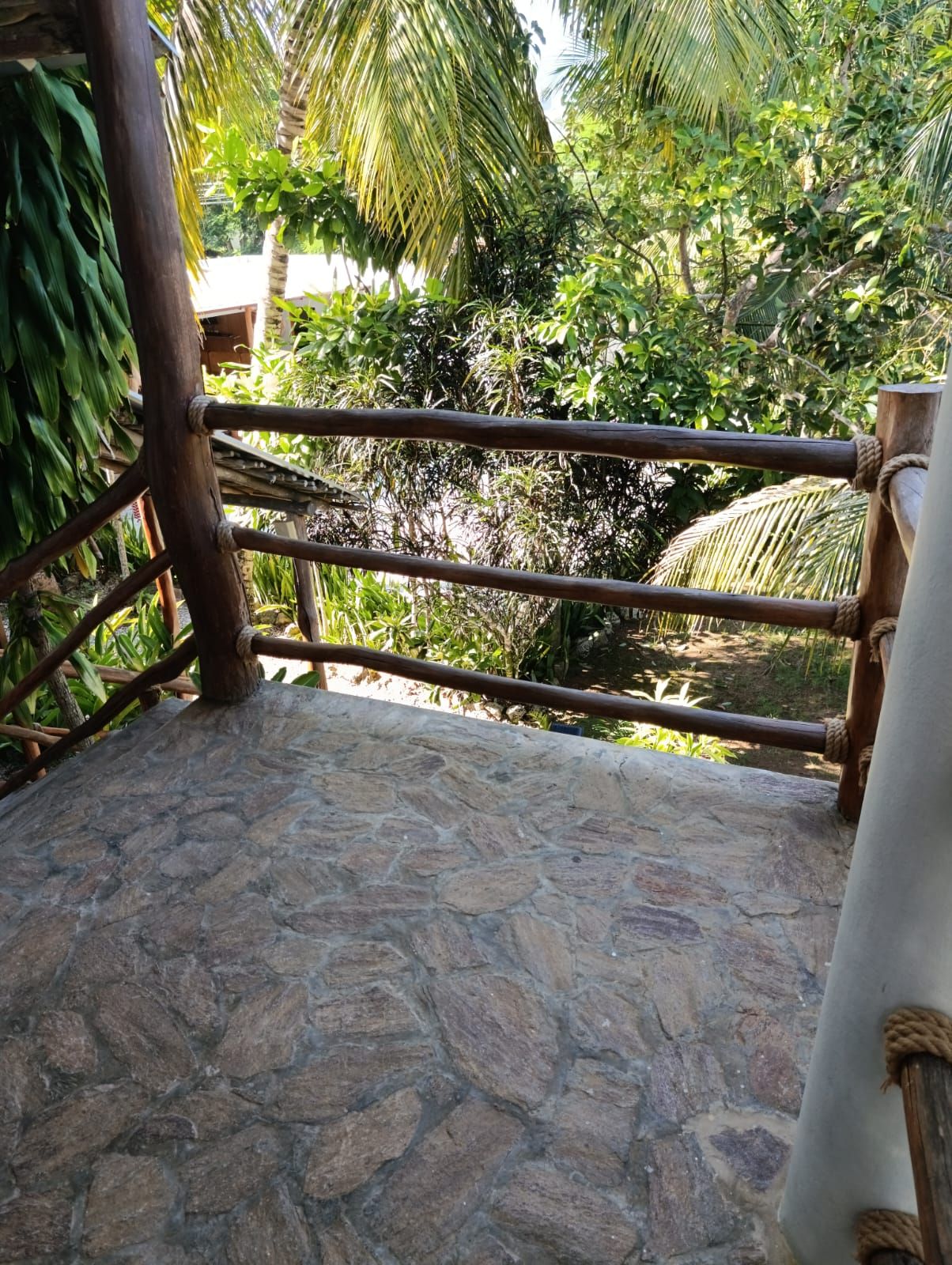 Un espacio al aire libre con suelo de piedra, barandilla de madera y amarres de cuerda.