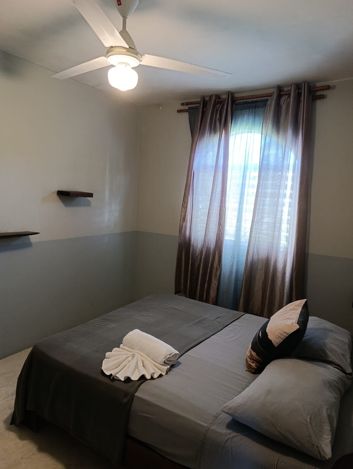 Un dormitorio con cama, ventilador de techo y ventana con cortinas.