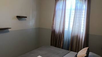 Un dormitorio con cama, ventilador de techo y ventana con cortinas.