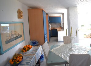 Une cuisine de taille réduite avec des meubles bleus, une table à manger recouverte d’une nappe blanche et un tableau encadré accroché au mur.