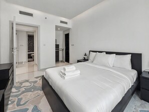 Une chambre à coucher moderne, avec un grand lit, une table de chevet et une salle de bain visible à travers une porte ouverte.