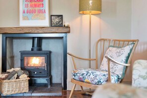 A cozy room with a wood-burning stove, a wicker basket, and a floral-patterned chair. - Charming, Stylish Cottage 15 mins from Edinburgh. Dog friendly, cosy log burner (Lasswade)