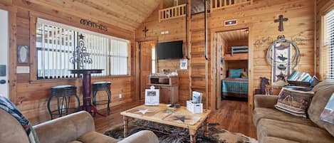 A cozy log cabin interior with a dining area, a television, and a living room furnished with sofas and a coffee table.