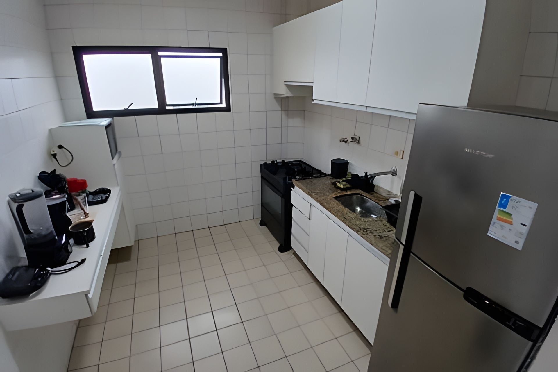 A compact kitchen with white cabinets, a stainless steel refrigerator, a gas stove, and a window above the sink.