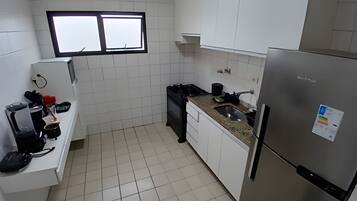 A compact kitchen with white cabinets, a stainless steel refrigerator, a gas stove, and a window above the sink.