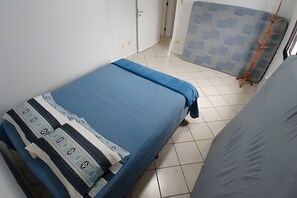 Een kleine, schone kamer met een bed, een kledingkast en een raam met zonwering.
