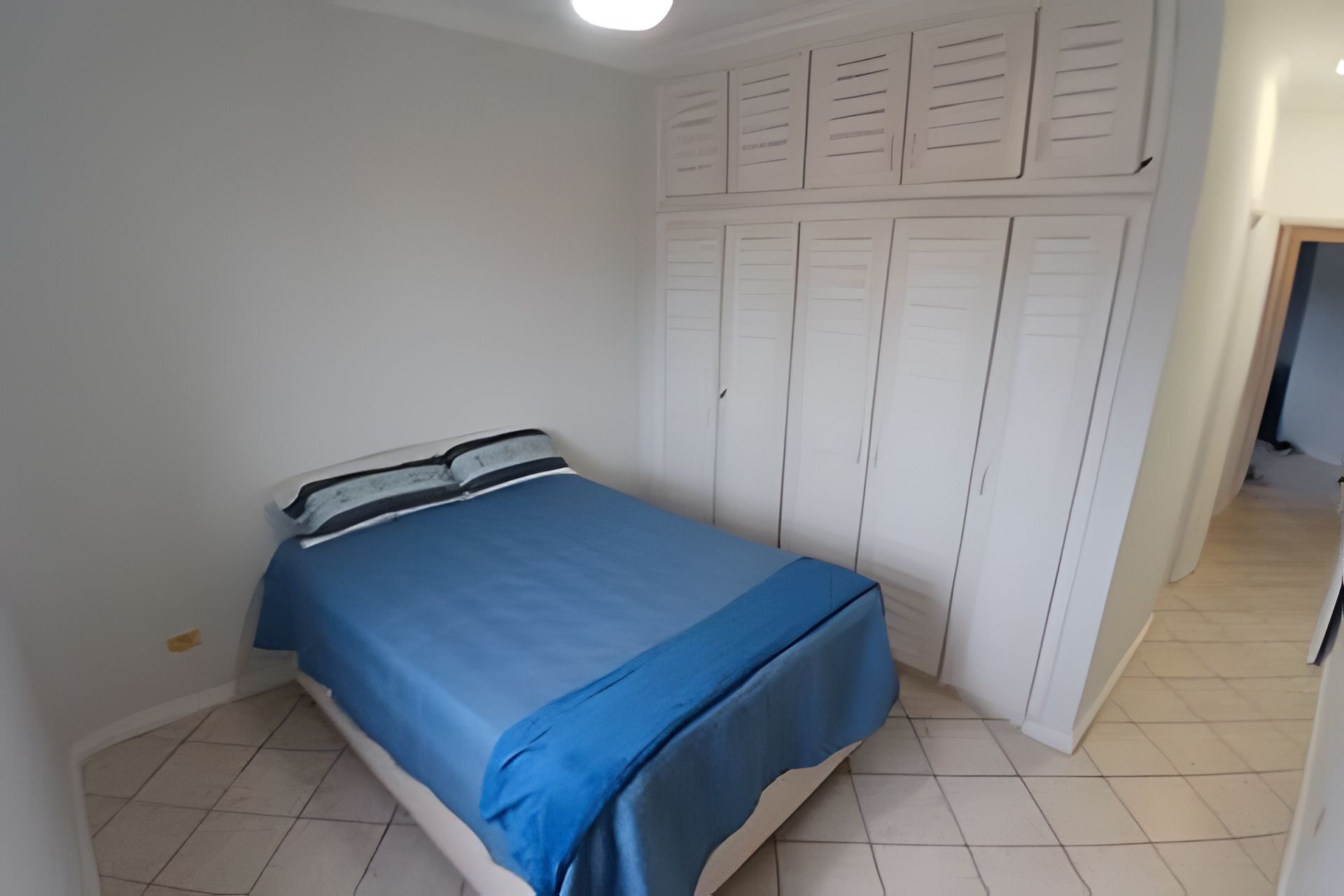 Ein Schlafzimmer mit einem Bett, einem weißen Wäscheschrank und einem Fliesenboden.