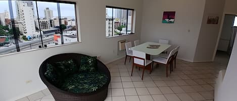 A spacious room with a large window, a dining table with chairs, a sofa, and a small kitchen area.