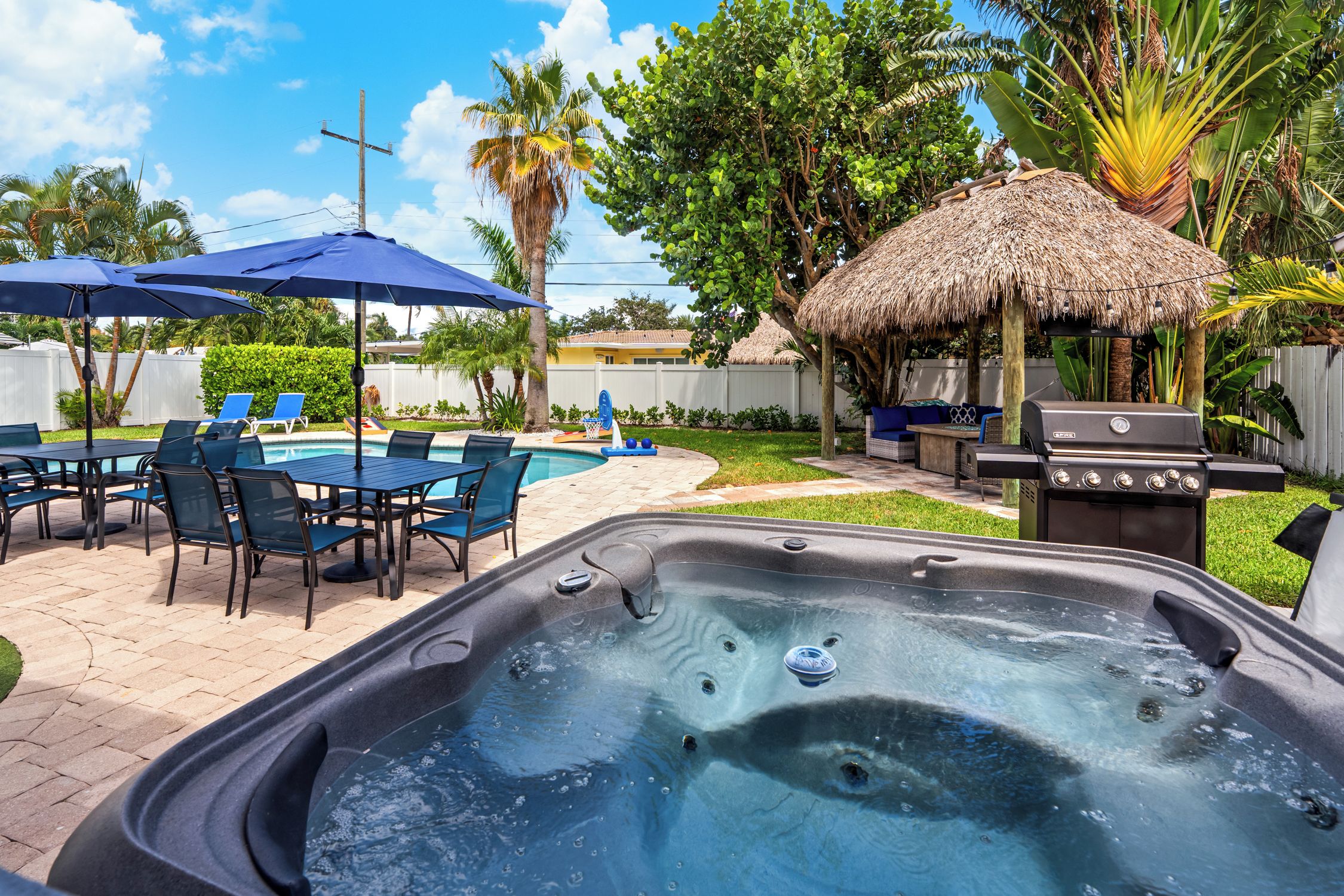 A backyard with a hot tub, outdoor seating, a barbecue grill, and a pool.